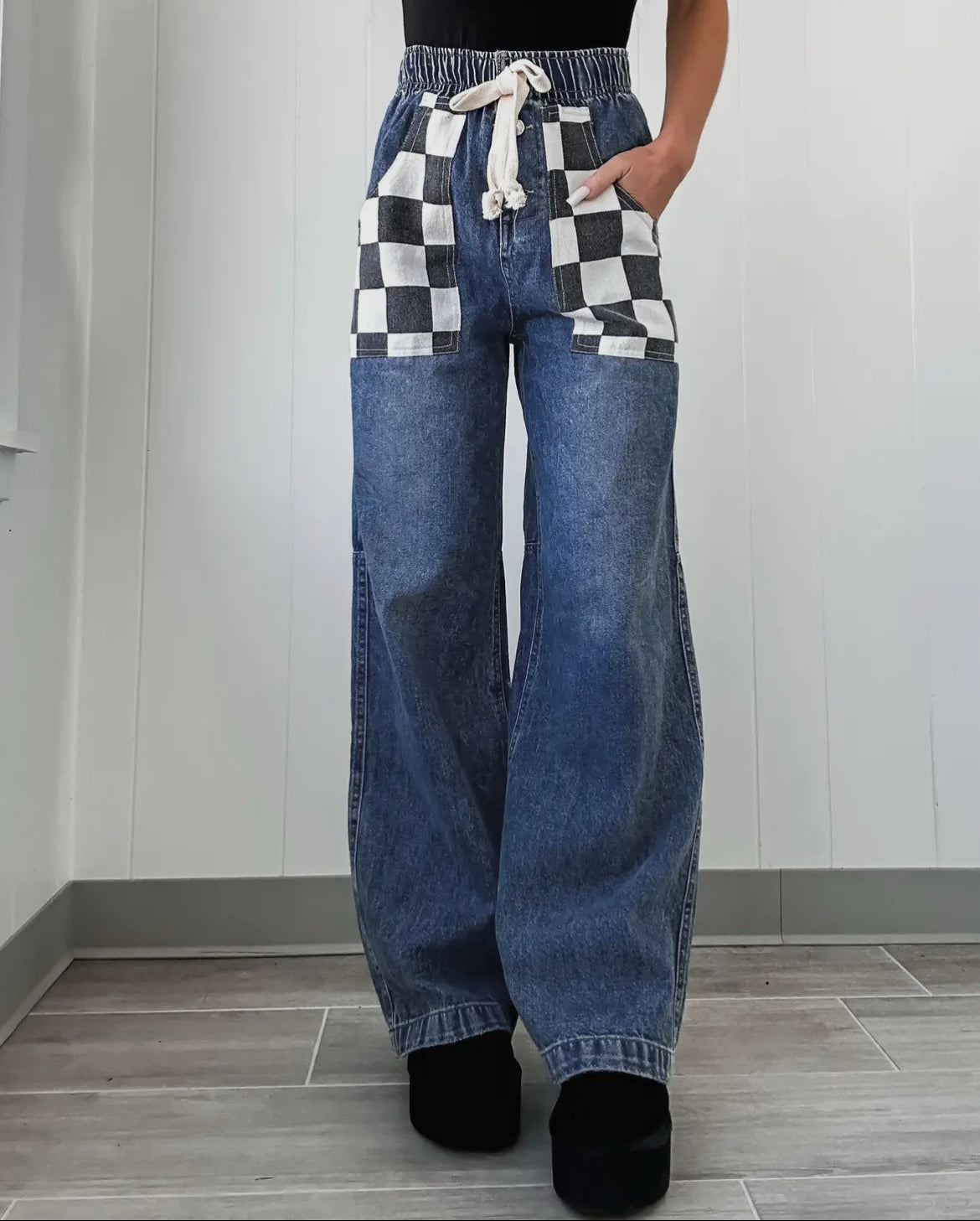 Person wearing blue jeans with checkered pockets against a white wall.
