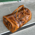 Brown leather duffel bag on a gray pavement